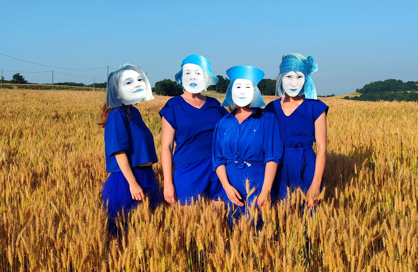 Photo de l'affiche du spectacle Roÿ-Roÿ, quatre femmes vêtues de bleu avec des masques en carton au milieu d'un champs de blé.