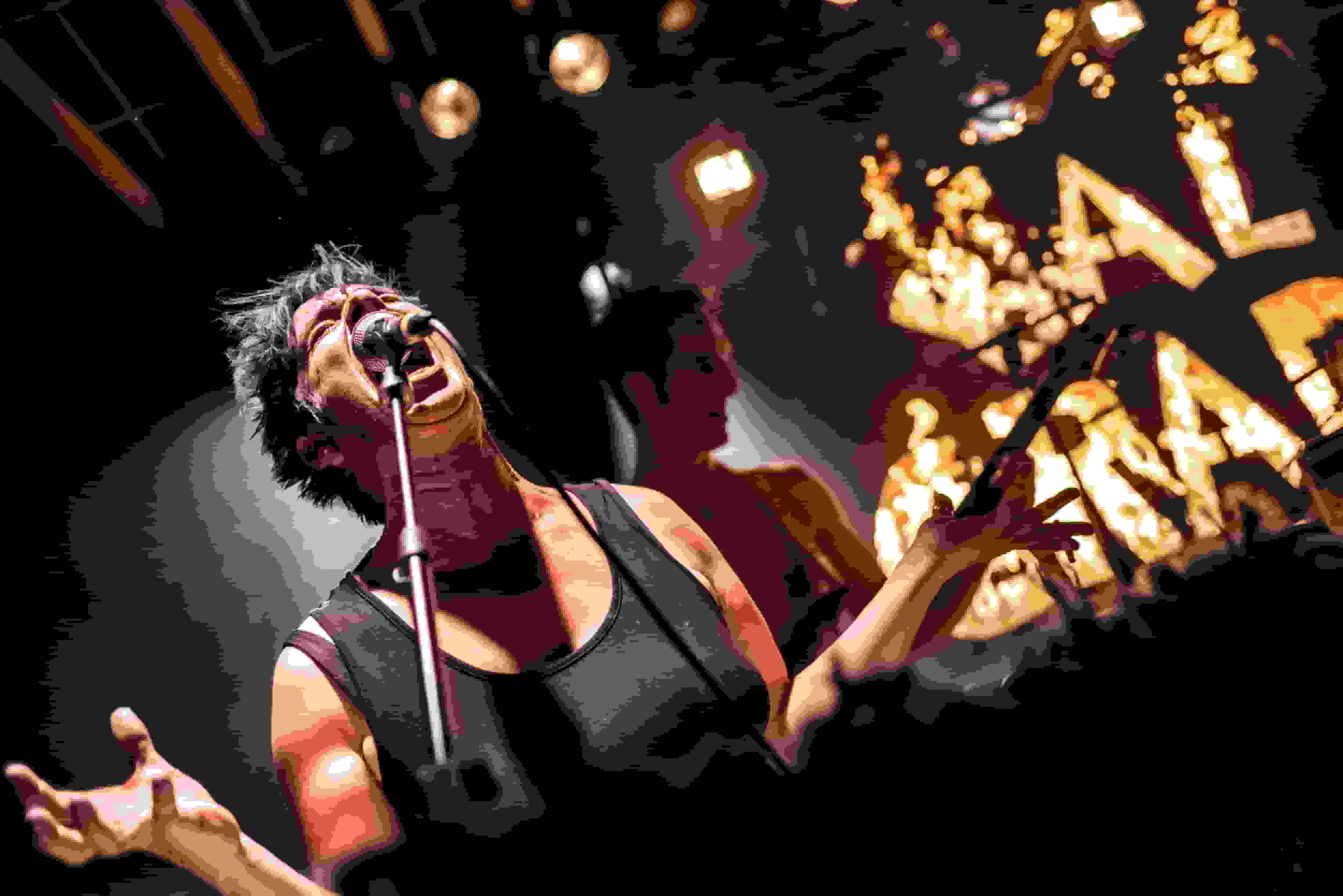 chanteuse, cheveux courts et bleus, qui hurle dans le micro, bras ouverts, avec à l'arrière scène les lettre BAL CRADE enflamées